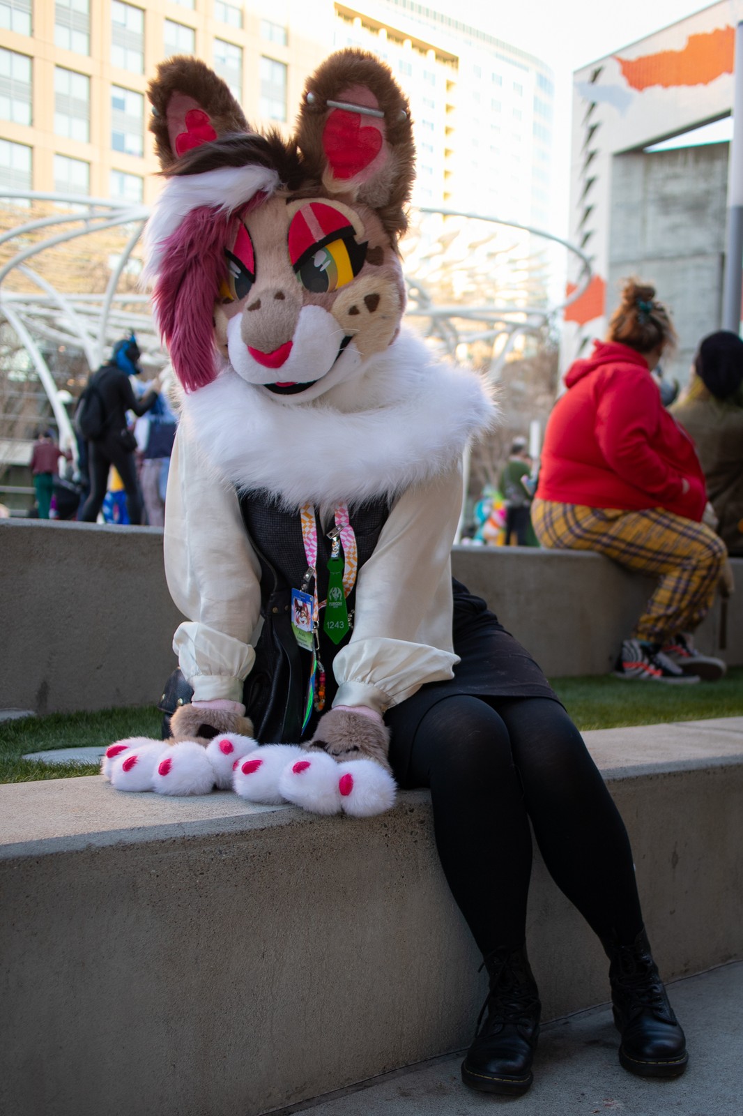 Hayan wearing her fursuit of Anais, a feminine rabbit. She sits on a concrete step outdoors.